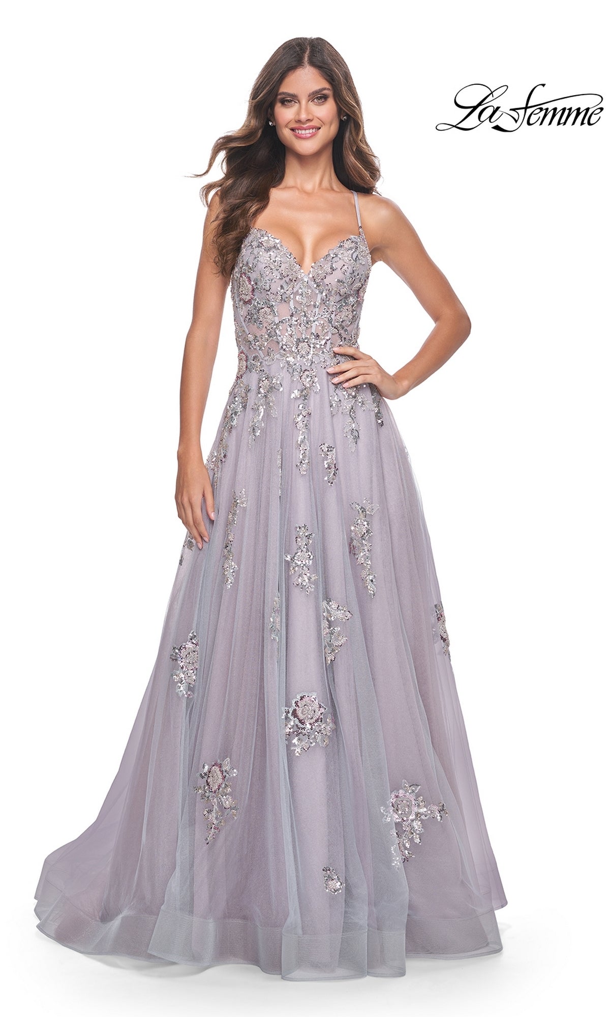 A woman stands against a white background wearing the La Femme Strappy-Back Long A-Line Prom Dress 32200 in lavender, featuring floral embellishments, thin straps, and a fitted bodice.